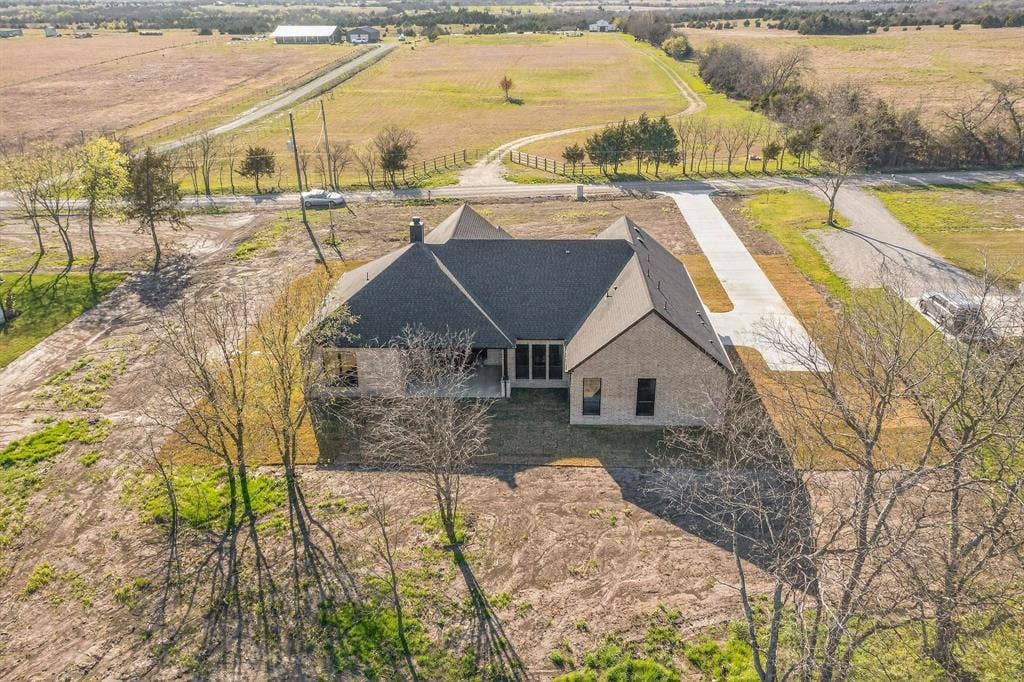 Single-story residence with a brick exterior, multi-gabled roof, covered rear patio, and a concrete driveway on an expansive lot