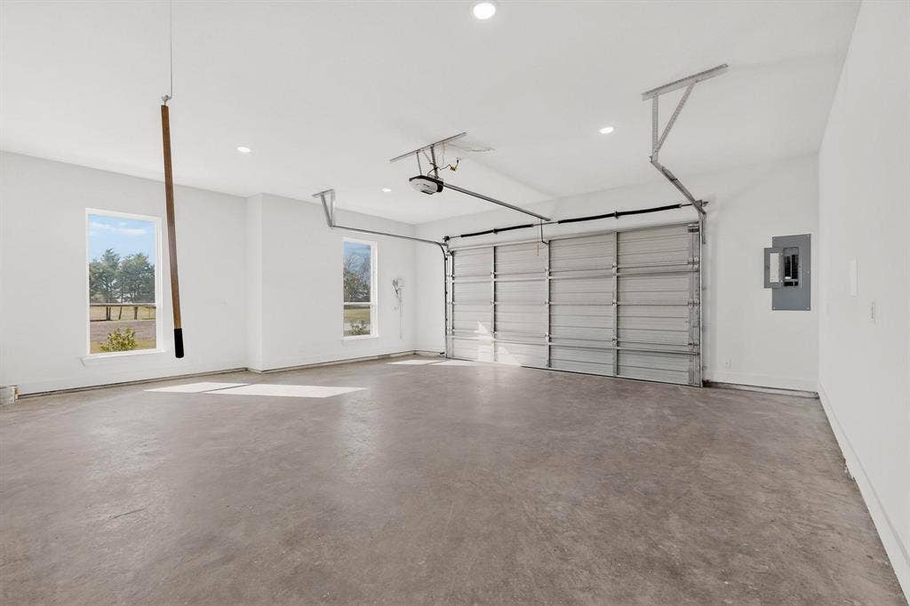 Spacious garage featuring finished walls, recessed lighting, concrete flooring, dual windows, and an automated overhead door system