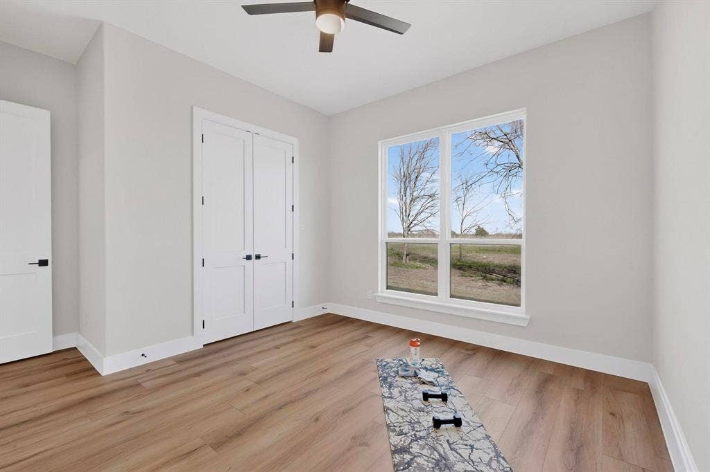 Interior space featuring wood-finish flooring, double-door closet with matte black hardware, dual-pane windows, and ceiling-mounted fan with integrated lighting