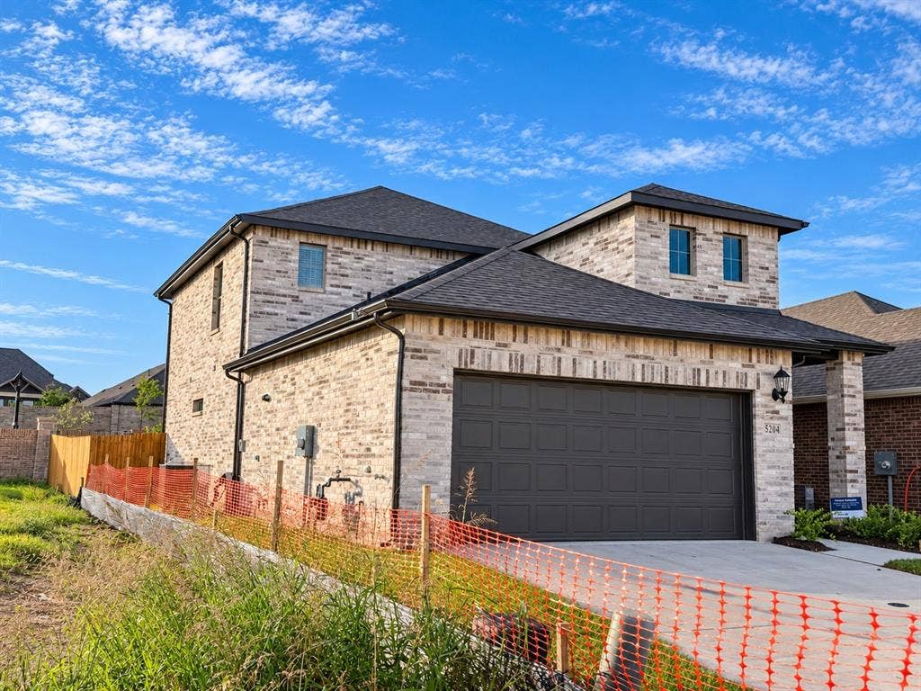 Two-story brick exterior featuring a multi-hipped roof, a paneled sectional garage door, and a concrete driveway