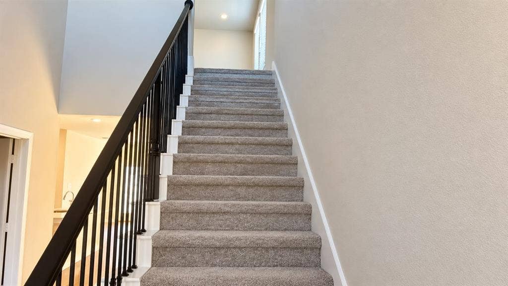 Staircase featuring wall-to-wall carpeting, black metal balusters, and a wooden handrail