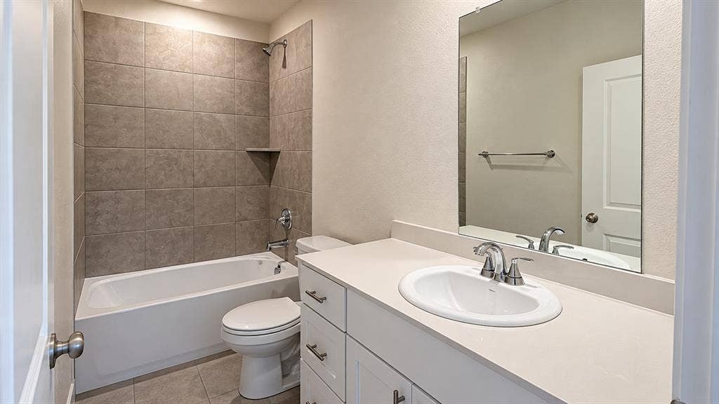 Full bathroom featuring white vanity cabinetry, solid-surface countertop with an integrated sink, polished chrome fixtures, and a shower-tub combination with oversized tile surround