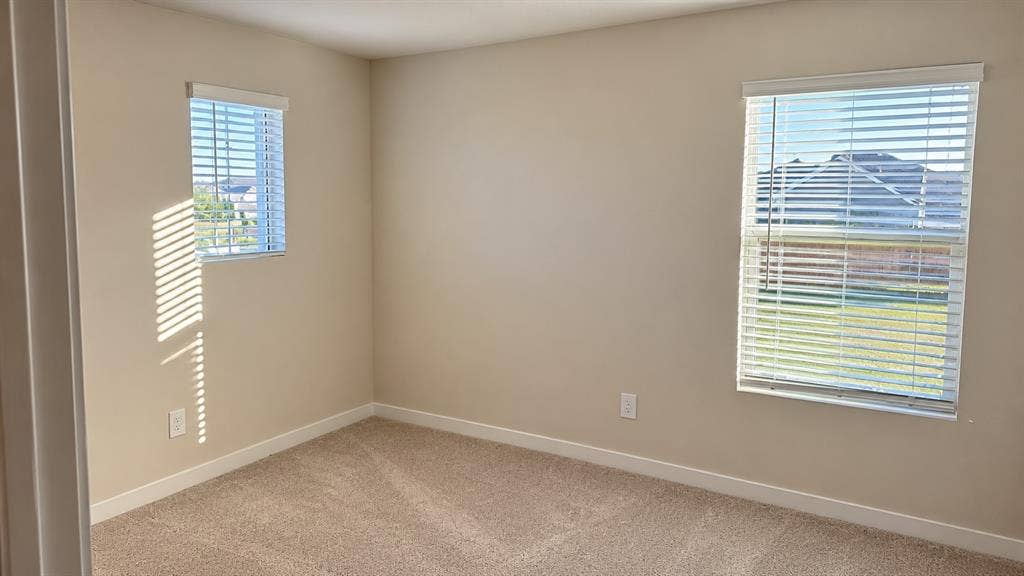 Neutral-toned interior space featuring wall-to-wall carpeting and dual windows equipped with horizontal blinds
