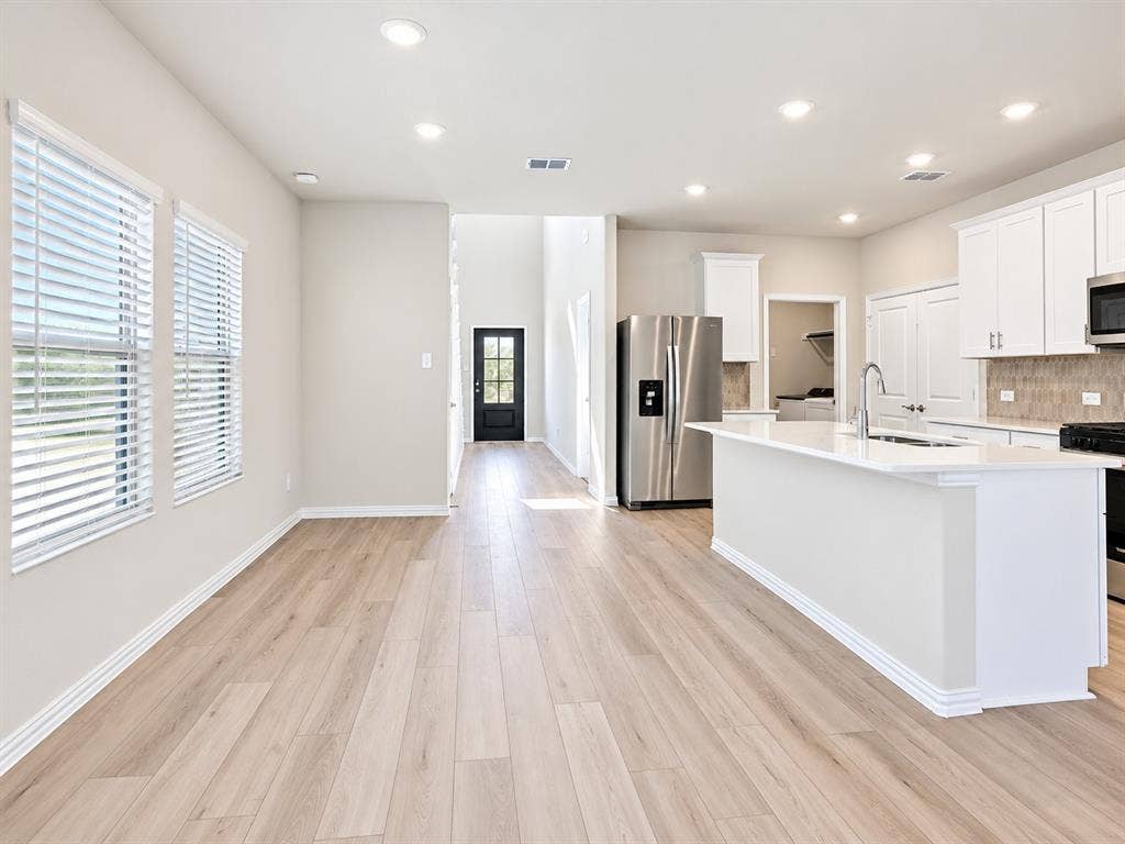 Open-concept living space featuring wood-finish flooring, recessed lighting, a kitchen island with a sink, stainless steel appliances, and white cabinetry
