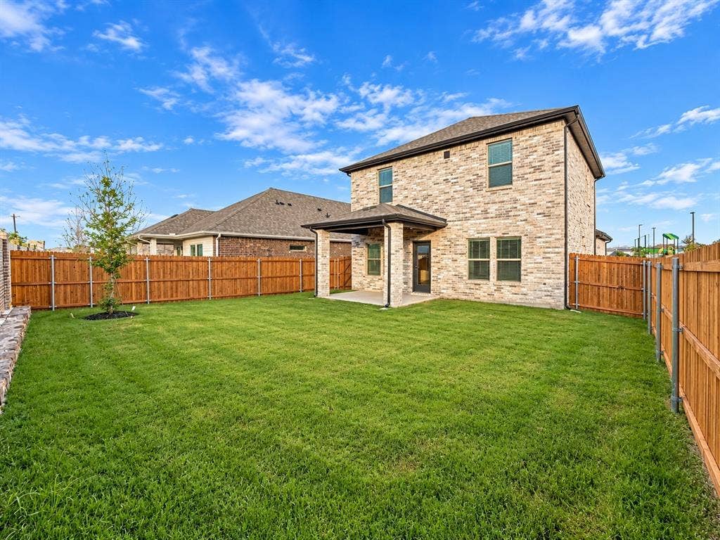 Two-story stone exterior featuring a covered rear patio, expansive sodded lawn, and full-perimeter wood fencing