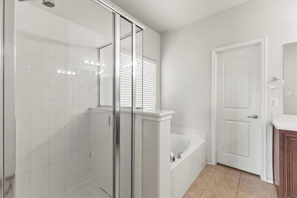Walk-in glass-enclosed shower featuring white tile surround, separate soaking tub with tiled deck, and neutral tile flooring