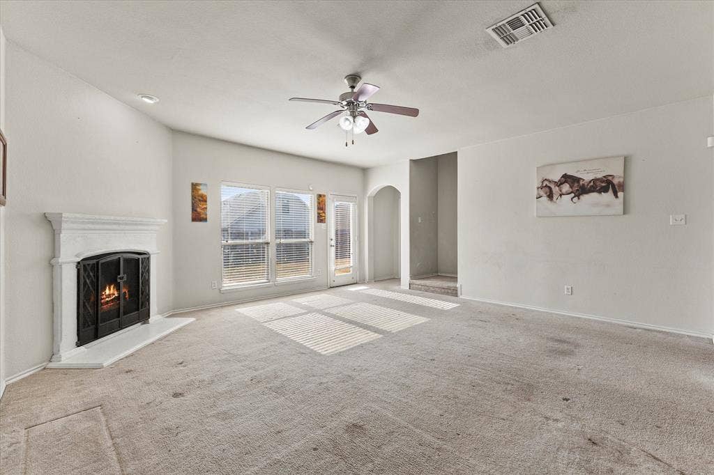 Living area featuring a fireplace with a white mantel, ceiling fan with integrated lighting, dual windows, and an arched entry