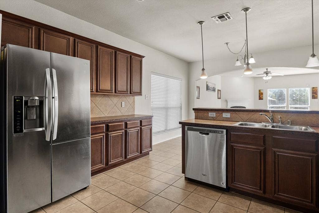 Kitchen featuring dark wood cabinetry, stainless steel appliances, tile backsplash, laminate countertops, and pendant lighting