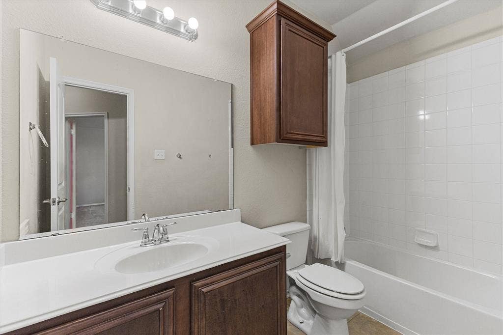 Bathroom featuring dark wood-finish cabinetry, a white countertop with an integrated sink, a wall-mounted storage cabinet, and a shower-tub combination with white tile surround