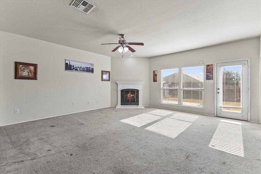 Corner fireplace with a white mantel, ceiling fan with light fixture, large windows, and a glass-paneled exterior door