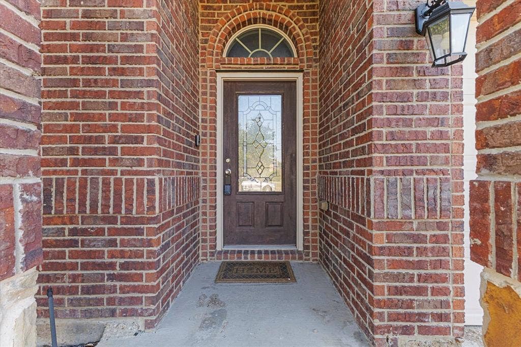 Entryway featuring red brick exterior siding, arched brick detailing with a semi-circular transom window, and a dark-finish wood door with glass inlay
