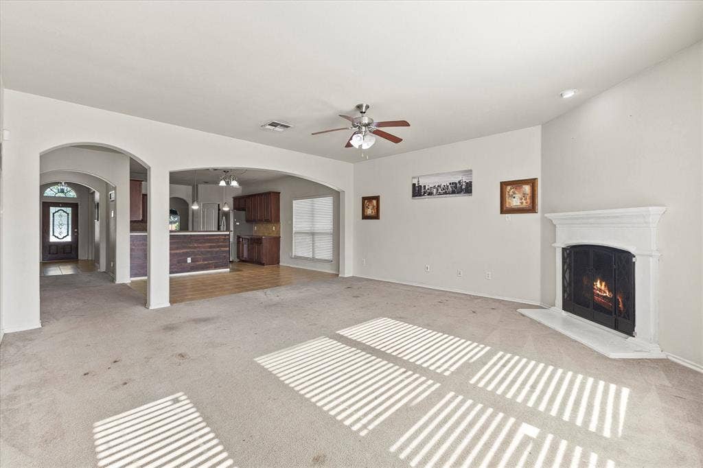 Living area featuring an arched entryway, recessed ceiling, fireplace with a white mantel, ceiling fan, and carpeted flooring