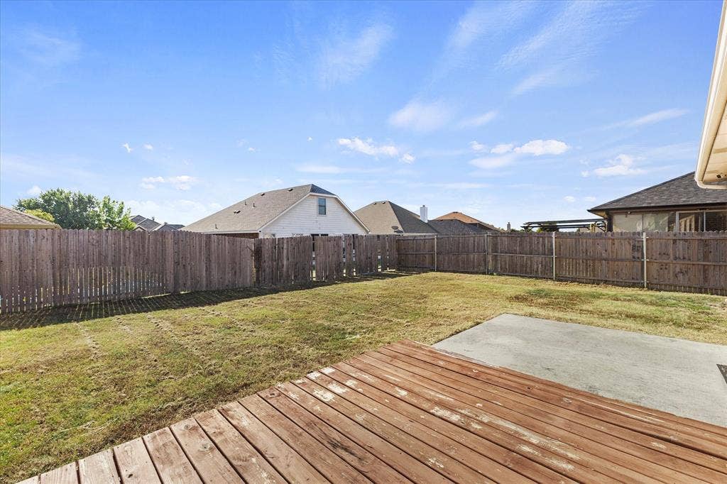 Rear exterior featuring a wood-plank deck, concrete patio, and fenced yard