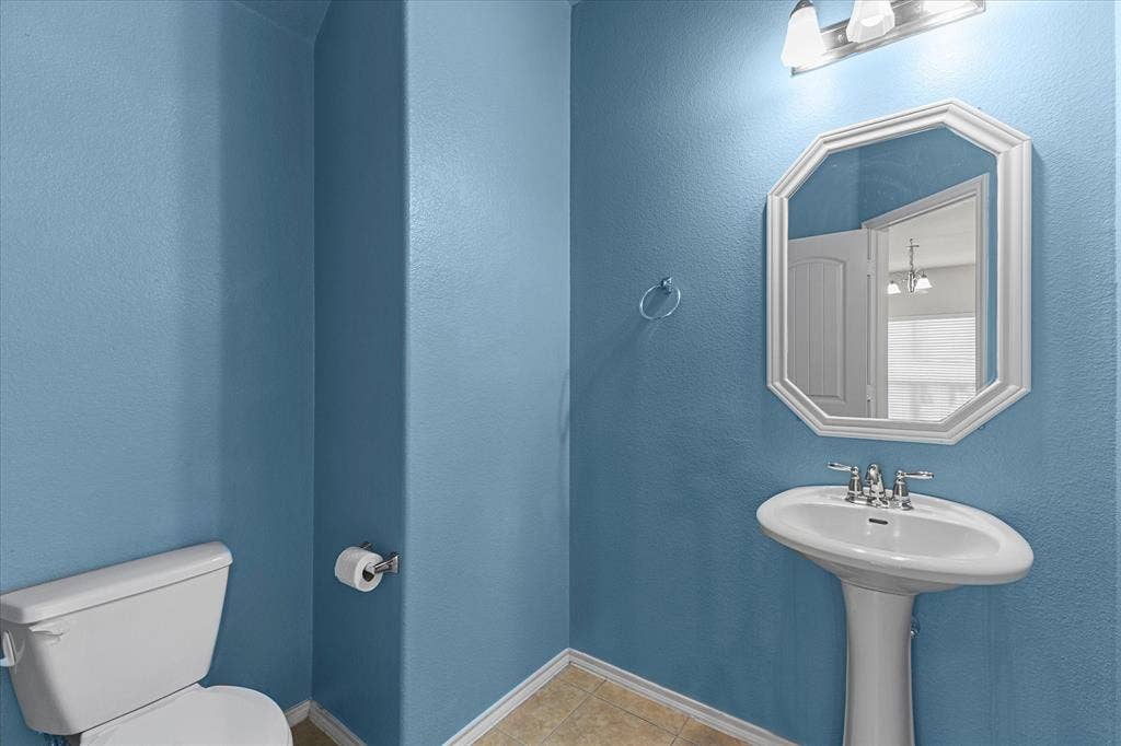 Powder room featuring a pedestal sink, wall-mounted light fixture, octagonal wall mirror, and tile flooring