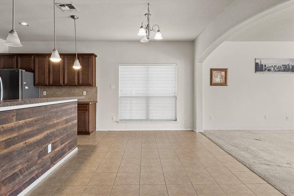 Kitchen featuring dark wood cabinetry, a breakfast bar with a wood-plank finish, tiled flooring, three pendant lights, and a central chandelier