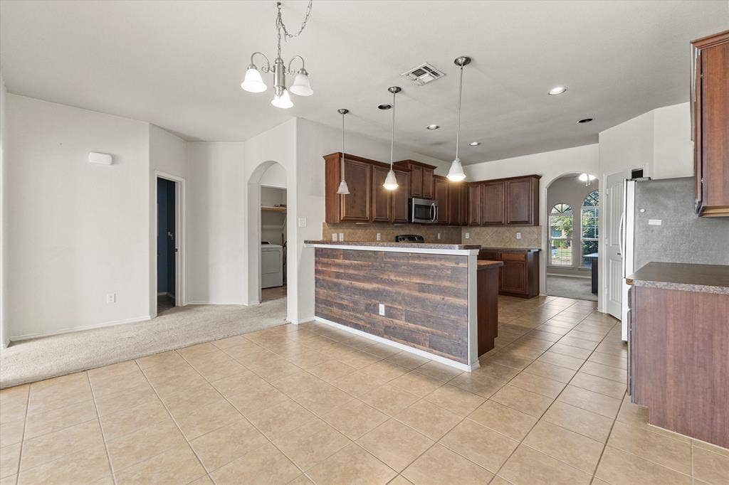 Kitchen featuring wood cabinetry, a breakfast bar with wood-plank surfacing, pendant lighting, tile flooring, and arched doorways