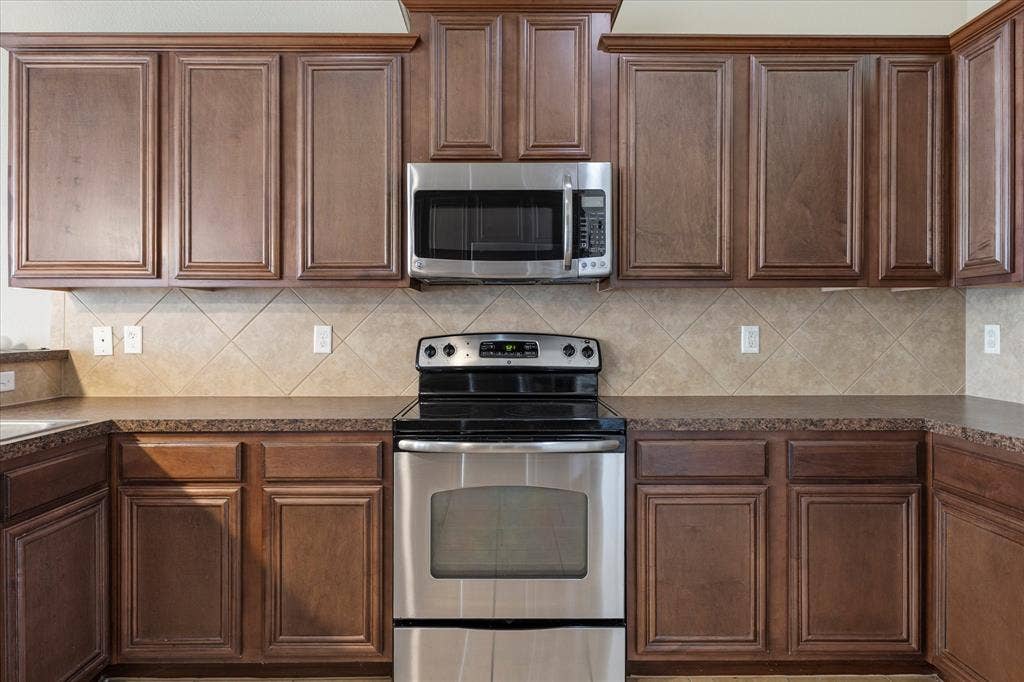 Kitchen featuring wood cabinetry with crown molding, stainless steel microwave, stainless steel range, and diagonal tile backsplash