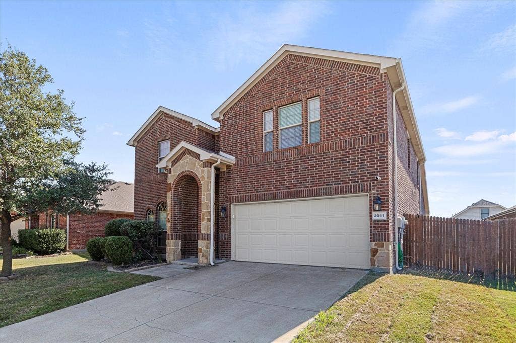 Two-story brick exterior featuring a stone-trimmed arched entryway, multi-paned windows, a two-car garage, and a wood privacy fence
