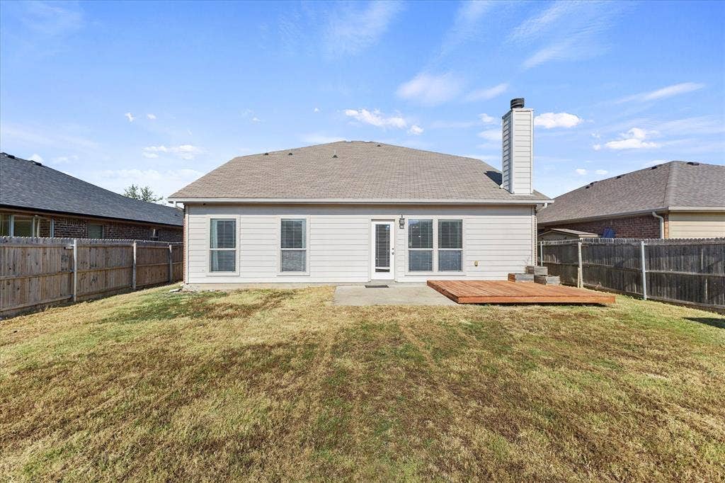 Rear exterior featuring horizontal siding, a masonry chimney, a concrete patio, a wood-finish deck, and wood privacy fencing