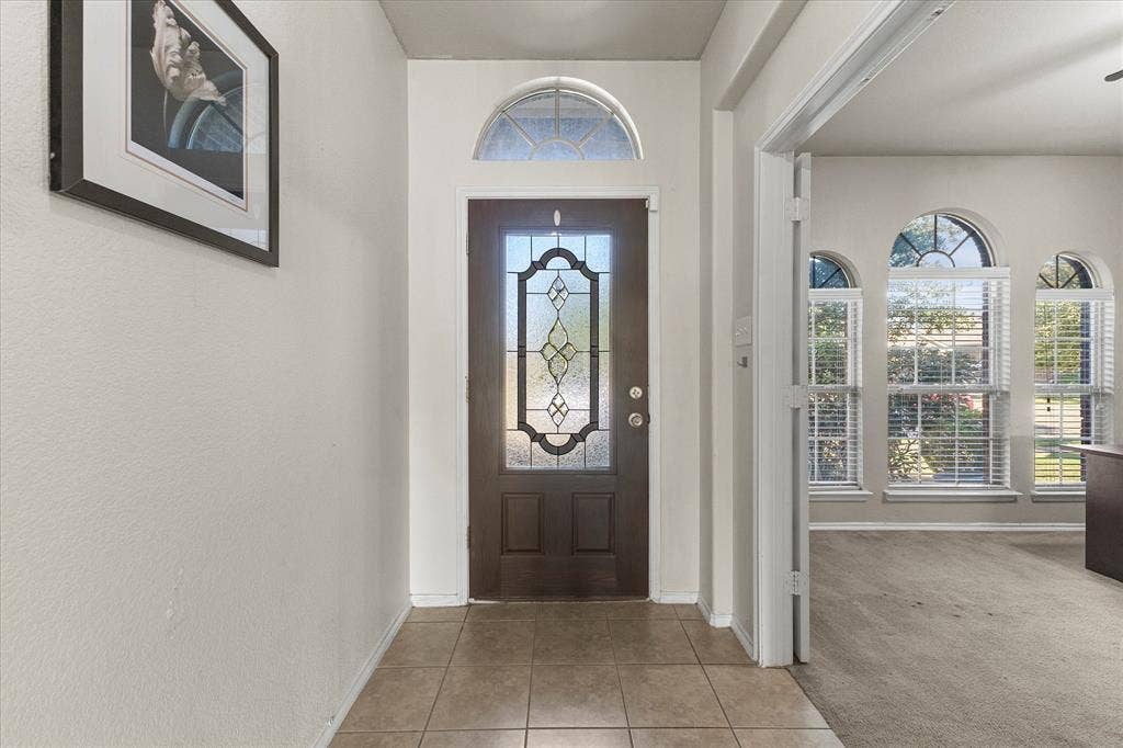 Entryway featuring a dark wood door with decorative glass inlay, an arched transom window, and neutral tile flooring