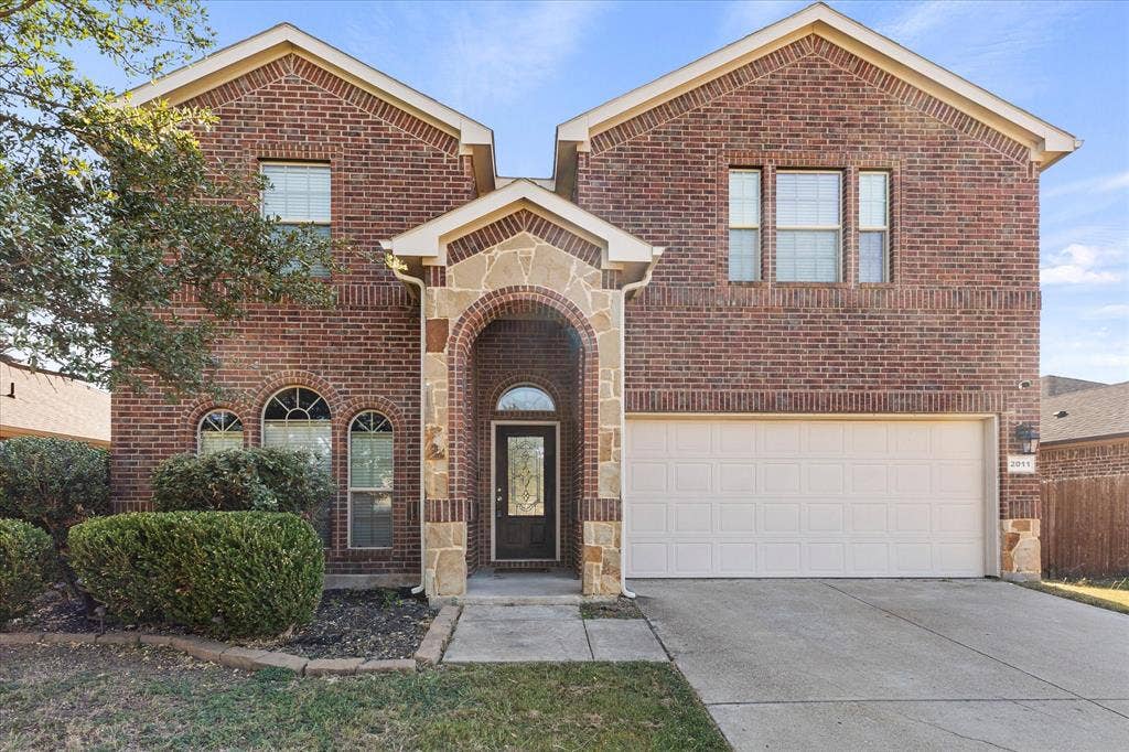 Two-story brick exterior featuring a stone-trimmed arched entryway, multi-pane windows, and an attached two-car garage