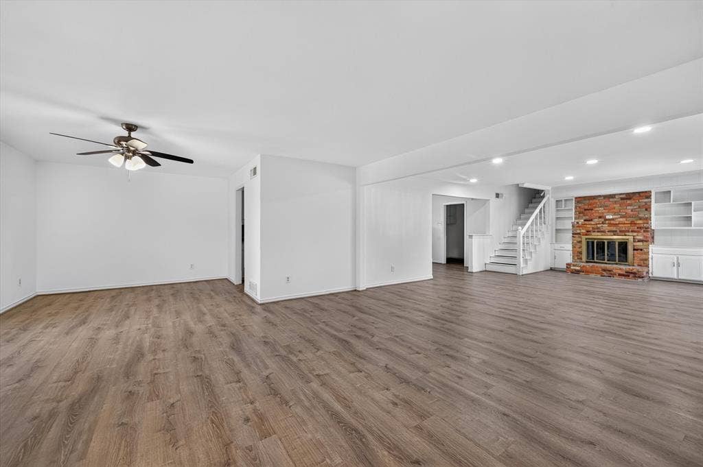 Open-concept living space featuring wood-finish flooring, recessed lighting, a ceiling fan, a floor-to-ceiling brick fireplace, and built-in shelving