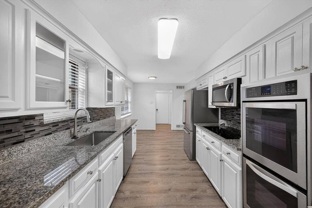 Kitchen featuring white shaker-style cabinetry, stone countertops, stacked-tile backsplash, wood-finish flooring, and stainless steel double wall ovens