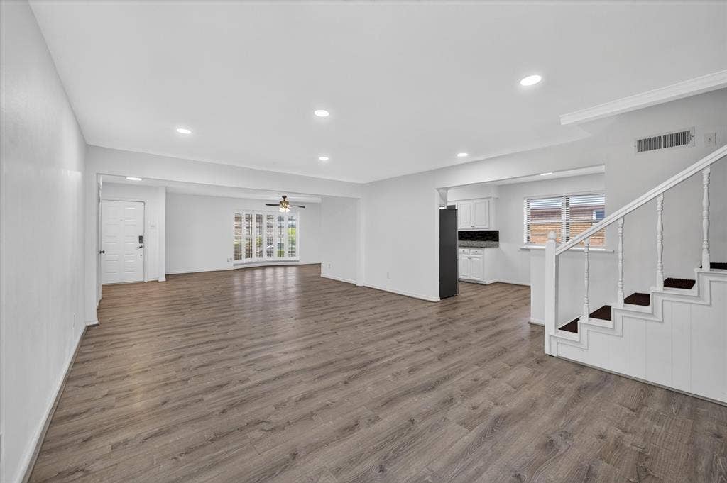 Open-concept interior featuring wood-finish flooring, recessed lighting, a multi-pane bay window, and a staircase with painted wood railings