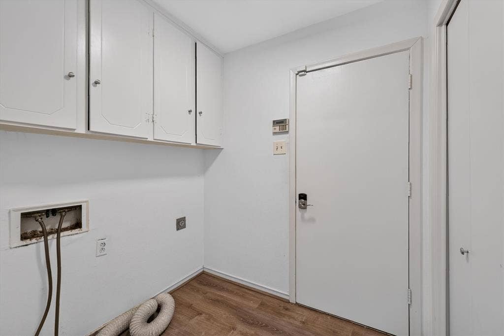 Utility area featuring wood-finish flooring, white upper wall-mounted cabinetry, and a solid-panel door with digital keypad entry