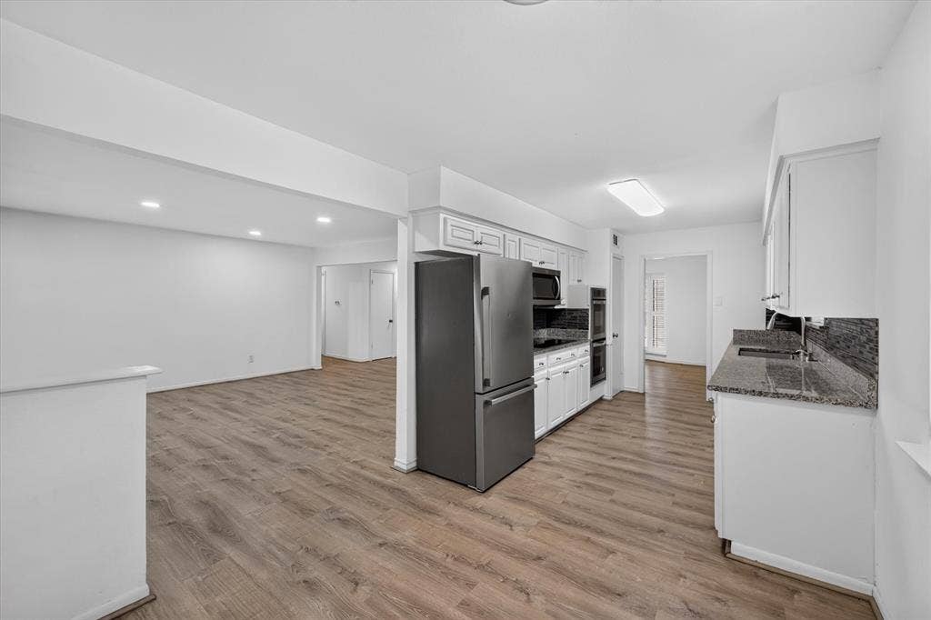 Kitchen featuring white cabinetry, stone-finish countertops, stainless steel refrigerator, and built-in double wall oven, finished with wood-finish flooring