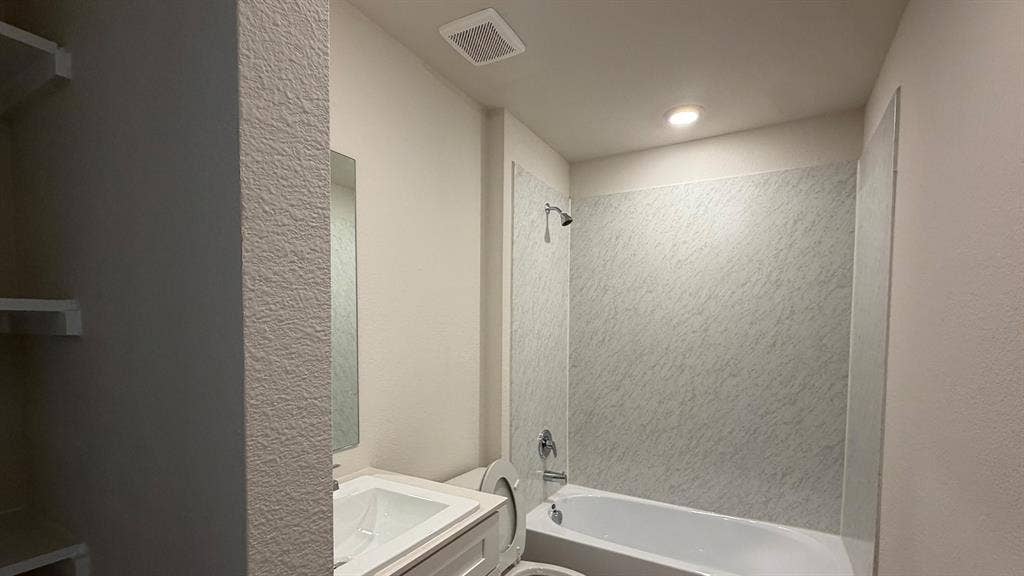 White tub and shower combination with textured wall surround, chrome fixtures, and recessed lighting