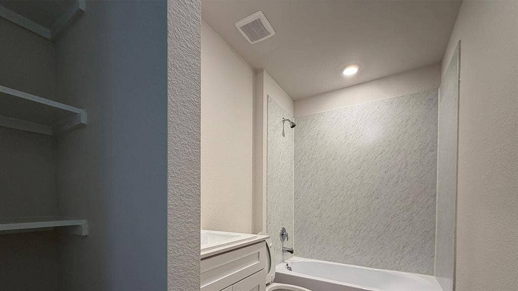 Bathroom featuring a white bathtub, patterned shower surround, and a chrome shower fixture