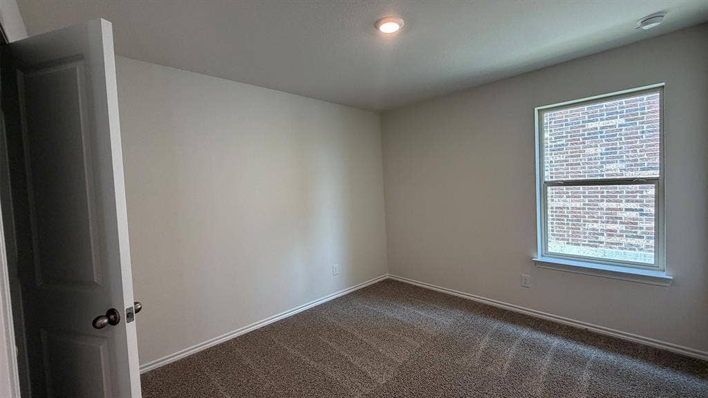Carpeted room featuring a single window with white trim, a recessed ceiling light, and a white interior door with a dark handle
