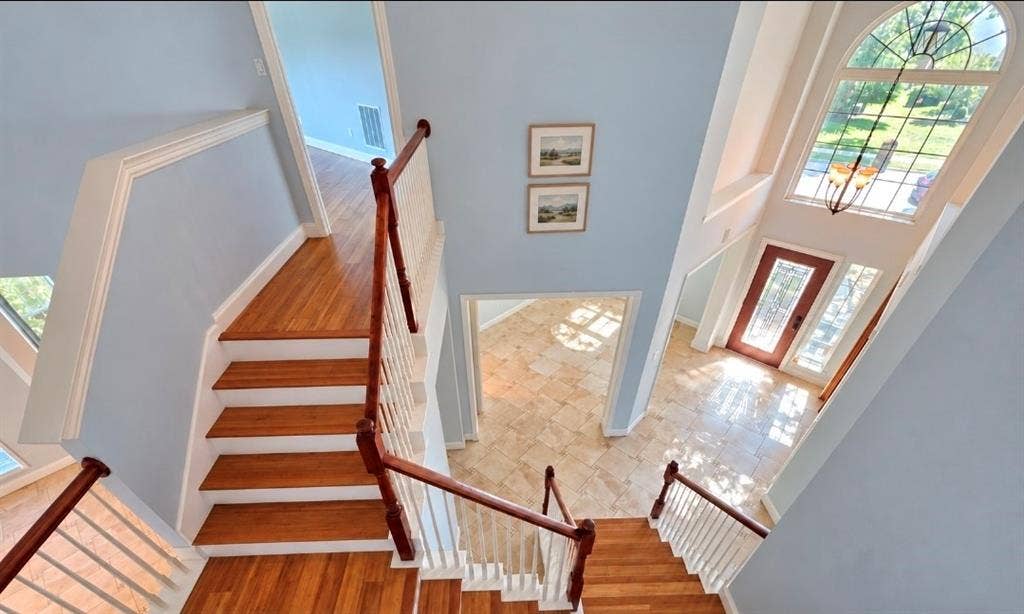 Foyer featuring tile flooring, a staircase with wood-finish treads, white balusters, and a decorative wood handrail, accented by an arched window with stained glass detail