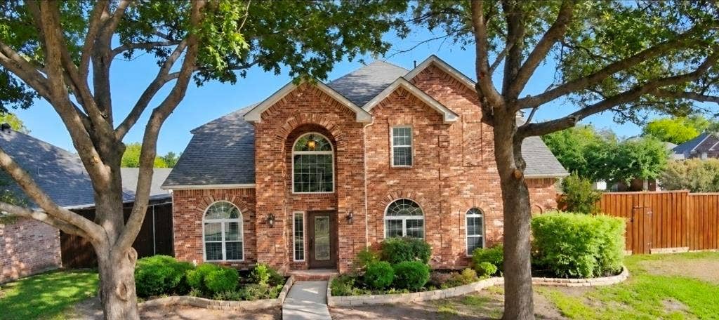 Two-story brick exterior featuring an arched entryway, decorative stone-edged landscaping, and a multi-gabled roofline