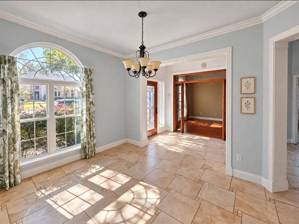 Arched window, tile flooring, crown molding, chandelier, and stained-wood cased entry