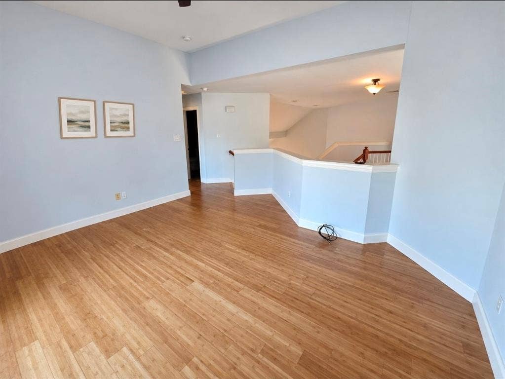 Open floor plan featuring wood-finish flooring, vaulted ceilings, and a wooden handrail staircase fixture