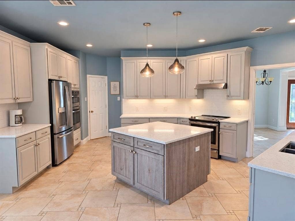 Kitchen featuring a central island with wood-finish cabinetry, quartz countertops, tile flooring, stainless steel appliances, and pendant lighting