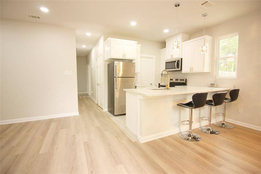 Kitchen featuring white cabinetry, wood-finish flooring, recessed lighting, stainless steel appliances, and a quartz countertop peninsula