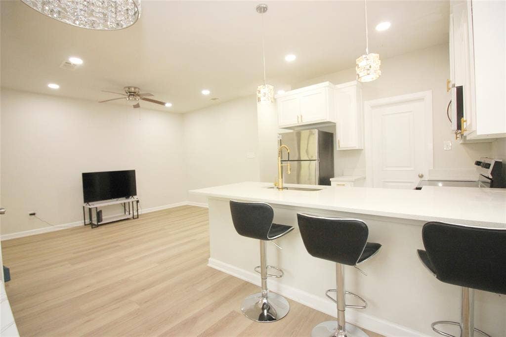 Kitchen featuring a quartz countertop island with a brass faucet, white shaker-style cabinetry, stainless steel appliances, pendant lighting, and wood-finish flooring