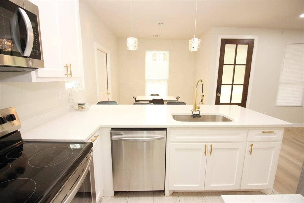 Kitchen featuring white shaker-style cabinetry, quartz countertops, stainless steel appliances, brass-finish hardware, and dual pendant lighting