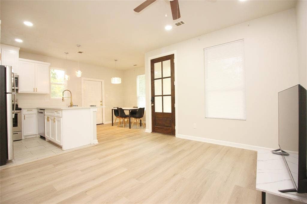 Open-concept kitchen featuring white shaker-style cabinetry, an island with stone-finish countertops, wood-finish flooring, recessed lighting, and a six-pane glass door with a stained wood finish