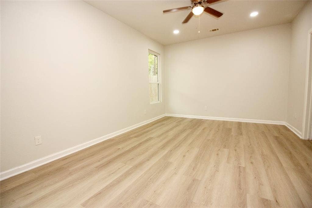 Neutral-toned interior featuring wood-finish flooring, recessed lighting, a ceiling fan with integrated light, and a single-pane window