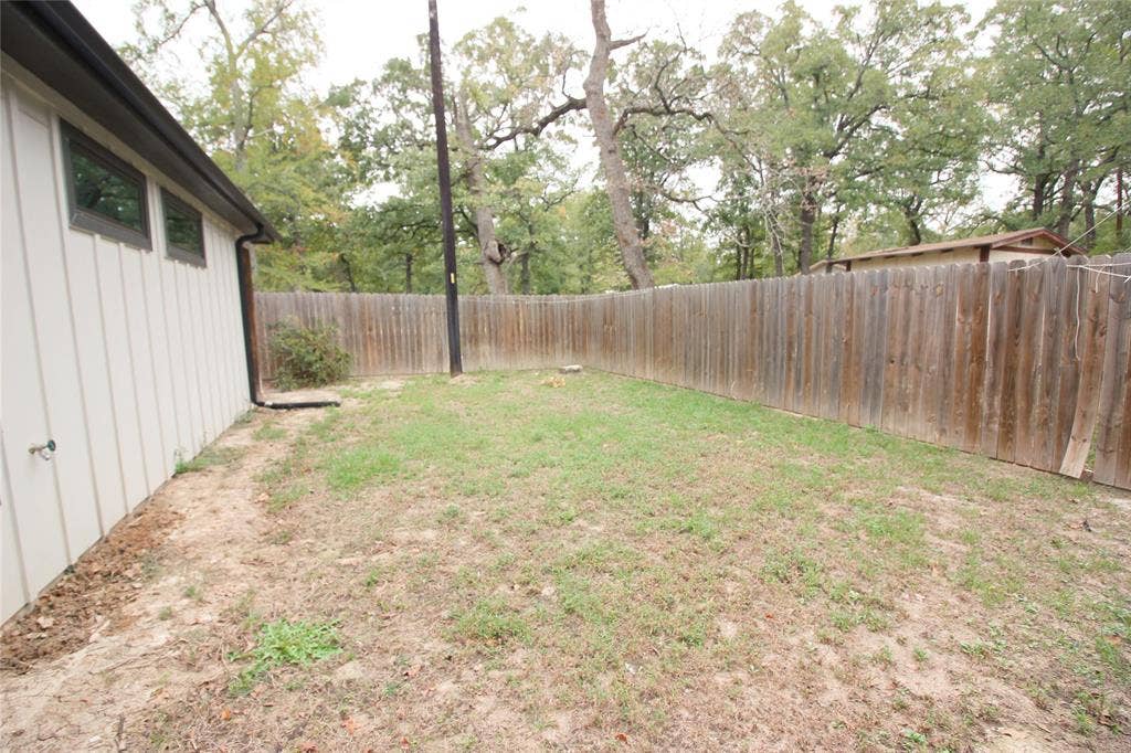 Exterior side yard featuring board and batten siding, horizontal wood privacy fencing, and mature trees