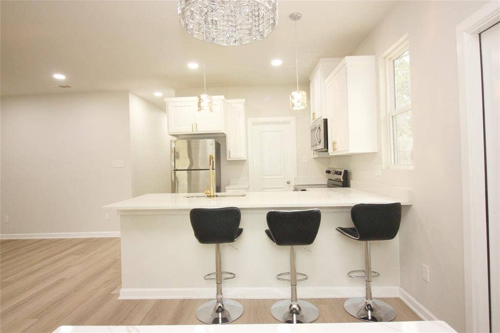 Kitchen featuring white cabinetry, quartz countertops, a breakfast bar, wood-finish flooring, and decorative pendant lighting