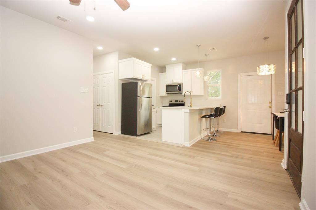Kitchen featuring white shaker-style cabinetry, stainless steel appliances, a peninsula counter with pendant lighting, and wood-finish flooring