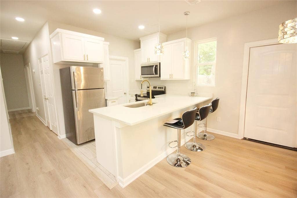 Kitchen featuring white cabinetry, solid-surface countertops, wood-finish flooring, stainless steel appliances, and a gooseneck faucet