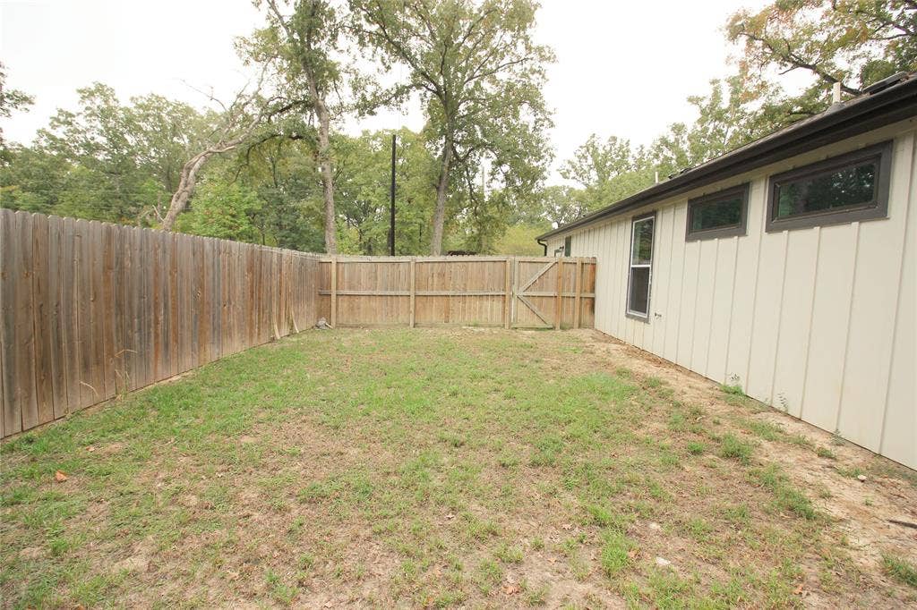 Backyard featuring vertical board siding, a wood privacy fence, and mature trees
