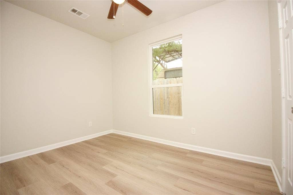 Neutral-toned interior featuring wood-finish flooring, a single-pane window, and a ceiling fan with integrated lighting