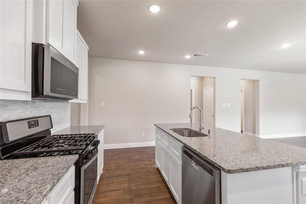 1253 Carinna Drive, Anna, TX 75409 Kitchen featuring white cabinetry, stone countertops, stainless steel appliances, a center island with a built-in sink, and wood-finish flooring